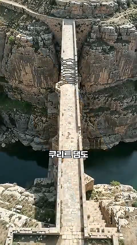 가파른 바위 절벽 사이에 세워진 좁고 긴 고대 돌 댐의 조감도.