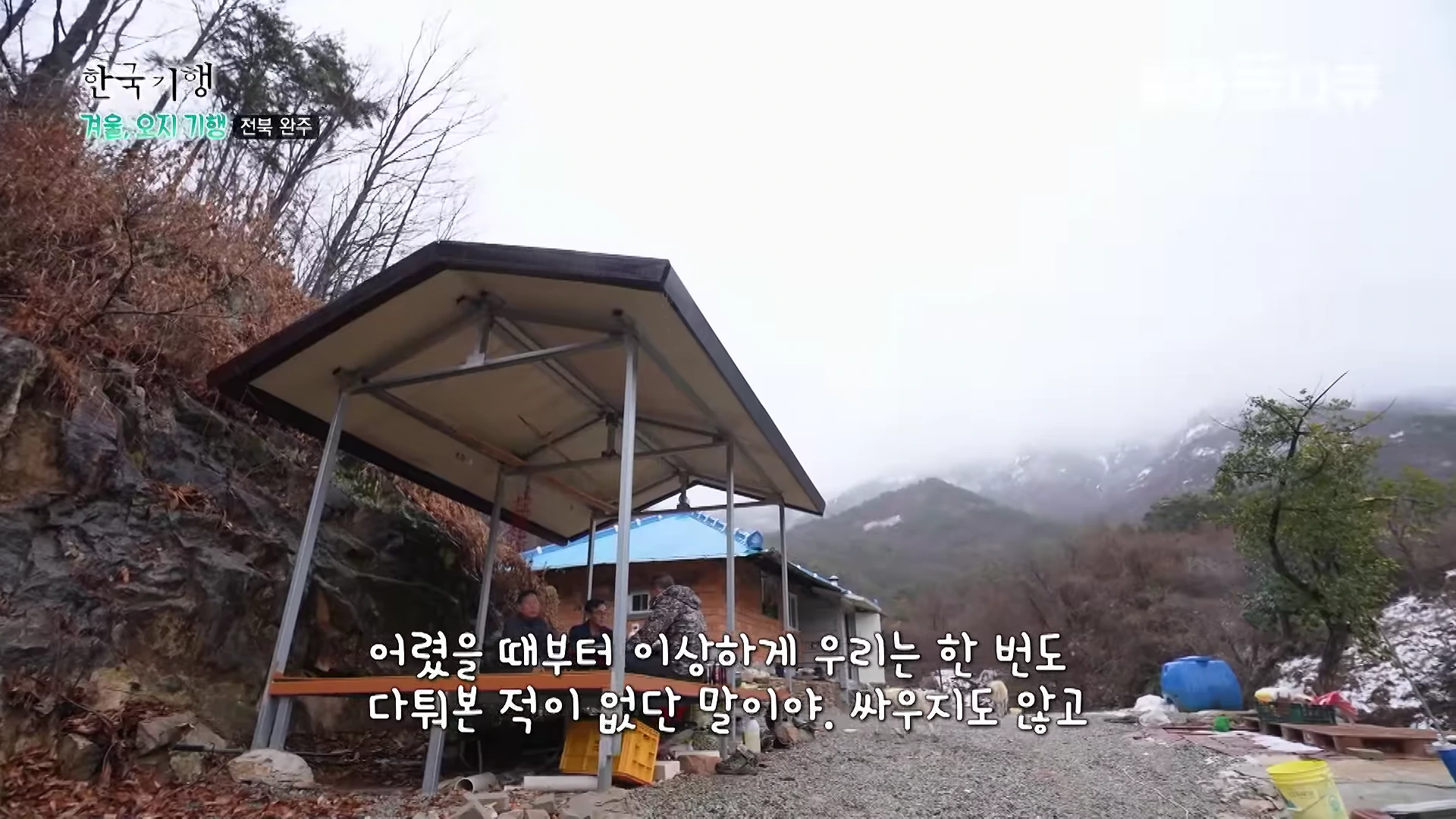 눈 덮인 산골 마을에 지붕이 있는 평상에 앉아 담소를 나누는 중년 남성들 모습