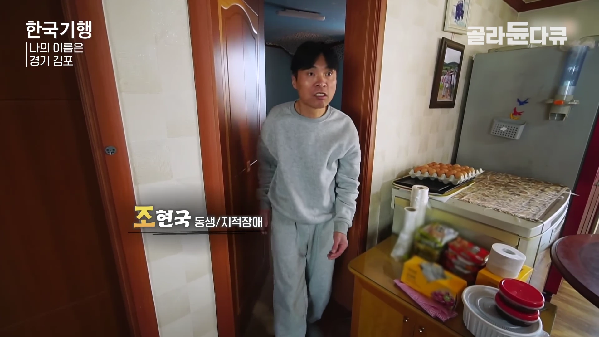 실내에서 회색 트레이닝복 차림의 남성이 문을 열고 걸어 나오고 있다. 왼쪽 하단에는 '조현국 동생/지적장애'라는 자막이 표시되어 있다.