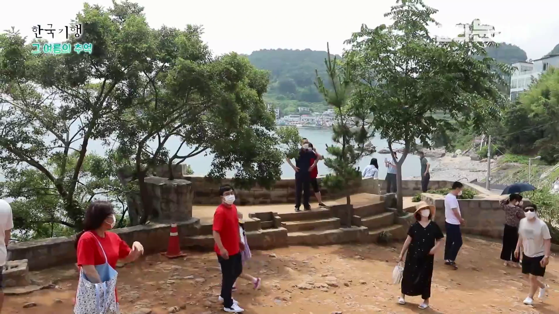 바닷가 언덕 위에 조성된 매미성 광장을 걷고 있는 관광객들의 모습. 마스크를 쓴 사람들이 계단과 평지가 섞인 돌길을 따라 움직이고 있으며, 뒤편으로는 바다와 나무들이 보인다.