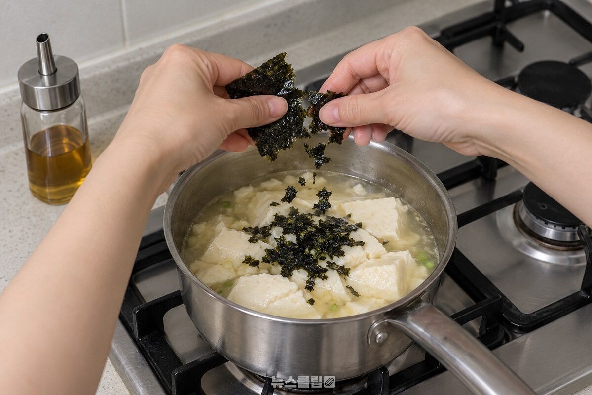 불을 끈 순두부국 위에 구운 김을 부수어 올리는 손 / 기사 이해를 돕기 위한 생성형 이미지