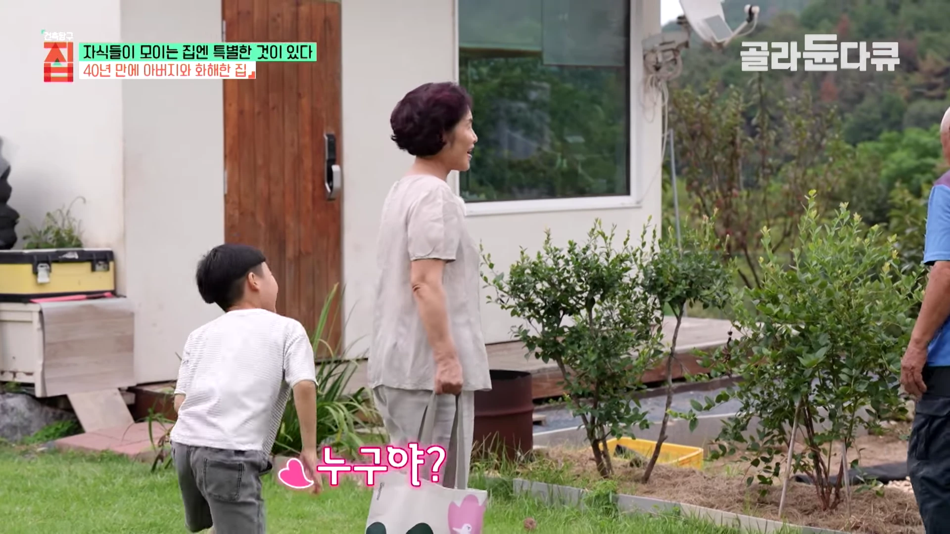 마당이 있는 하얀 집 앞마당에서 짧은 머리의 할머니가 손가방을 들고 서 있고, 옆에서 어린아이가 할머니를 쳐다보며 말을 건네고 있다. 오른편에는 푸른색 상의를 입은 노인의 모습이 일부 보인다.
