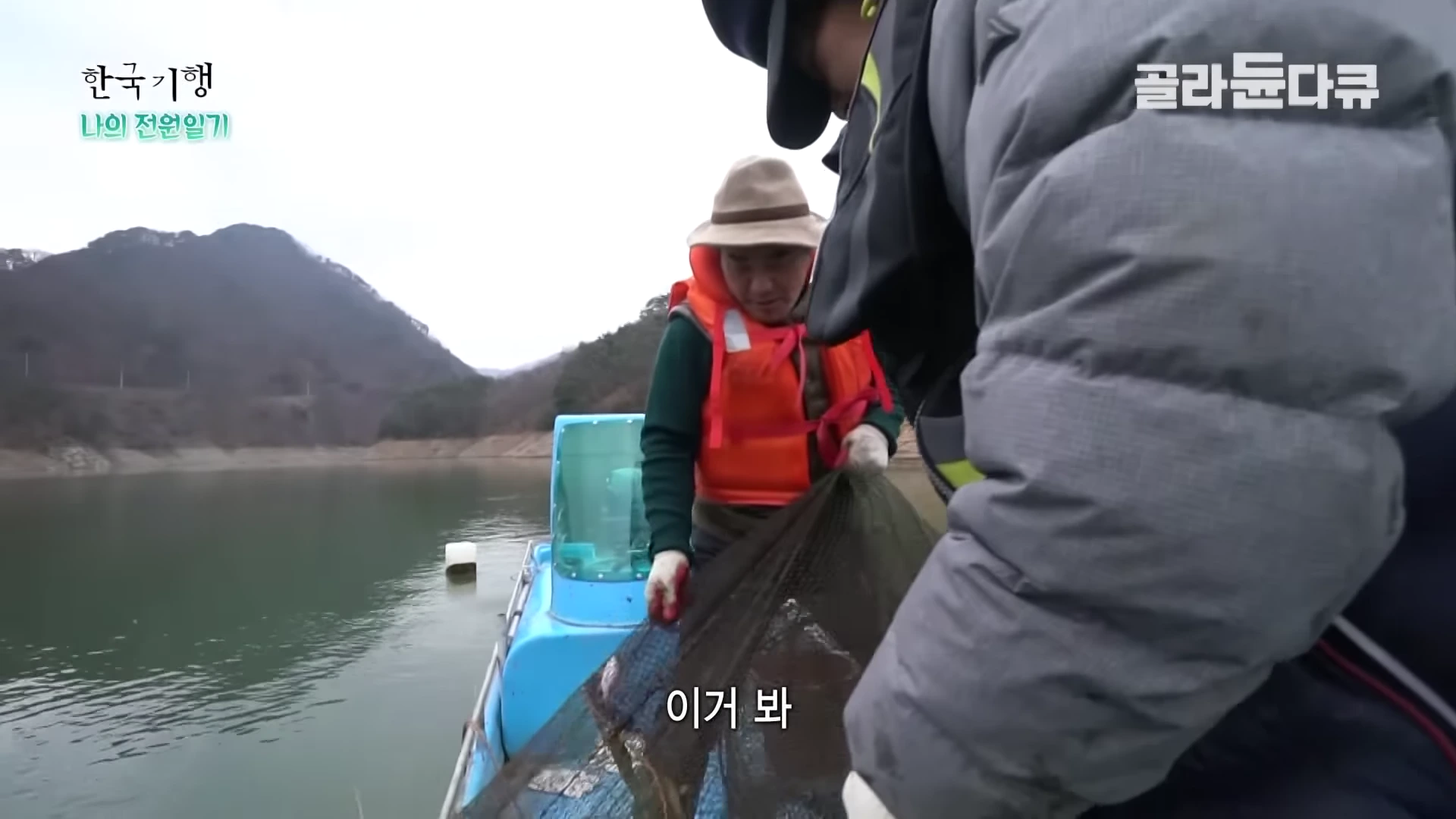 두 사람이 작은 배 위에서 그물을 끌어 올리며 고기를 확인하고 있는 모습