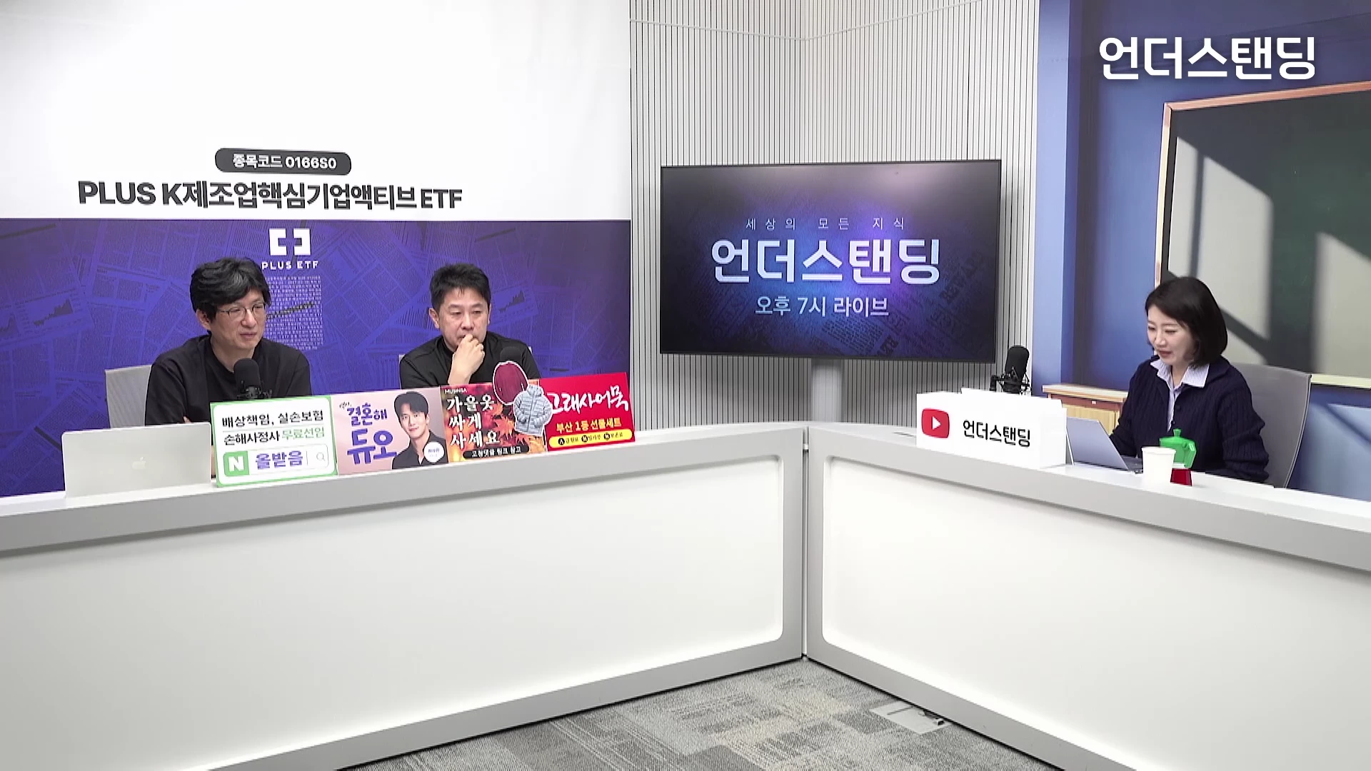 두 명의 남성과 한 명의 여성이 스튜디오의 흰색 긴 테이블에 앉아 대화하고 있으며, 뒤쪽 벽면에는 프로그램 이름이 표시된 대형 모니터가 배치되어 있습니다.