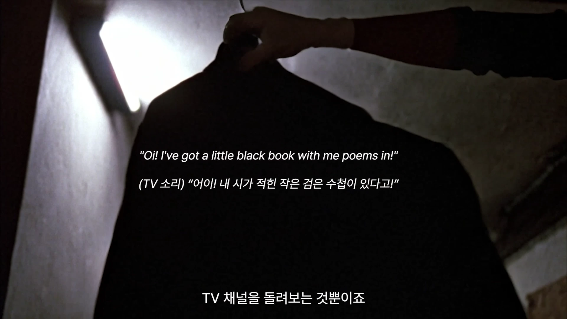 어두운 공간에서 옷걸이에 걸린 검은 옷을 한 손으로 잡고 있는 모습과 함께 영어와 한국어 자막이 화면 중앙에 배치된 영상 장면