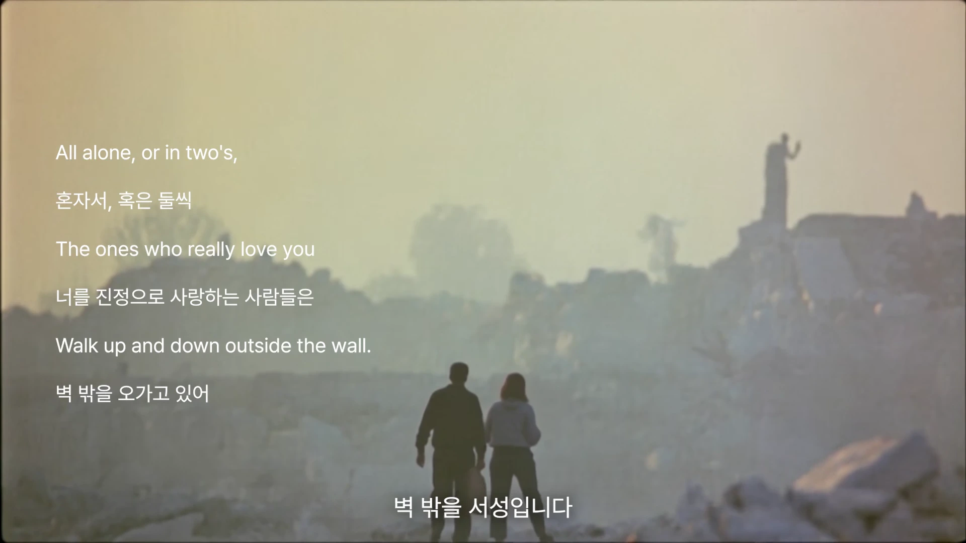 안개 자욱하고 황량한 폐허 속에서 뒷모습을 보이며 걸어가는 두 사람과 그 위에 영어와 한글로 된 자막이 겹쳐져 있는 영화의 한 장면.