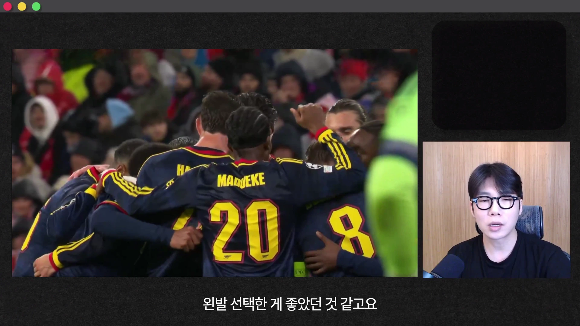 축구 경기 영상 프레임과 이를 해설하는 남성의 모습이 담긴 화면으로, 경기 영상에는 등번호 20번과 8번이 적힌 유니폼을 입은 선수들이 모여 기뻐하는 뒷모습이 보이고, 오른쪽 하단에는 안경을 쓴 남성이 마이크 앞에서 이야기하고 있다.