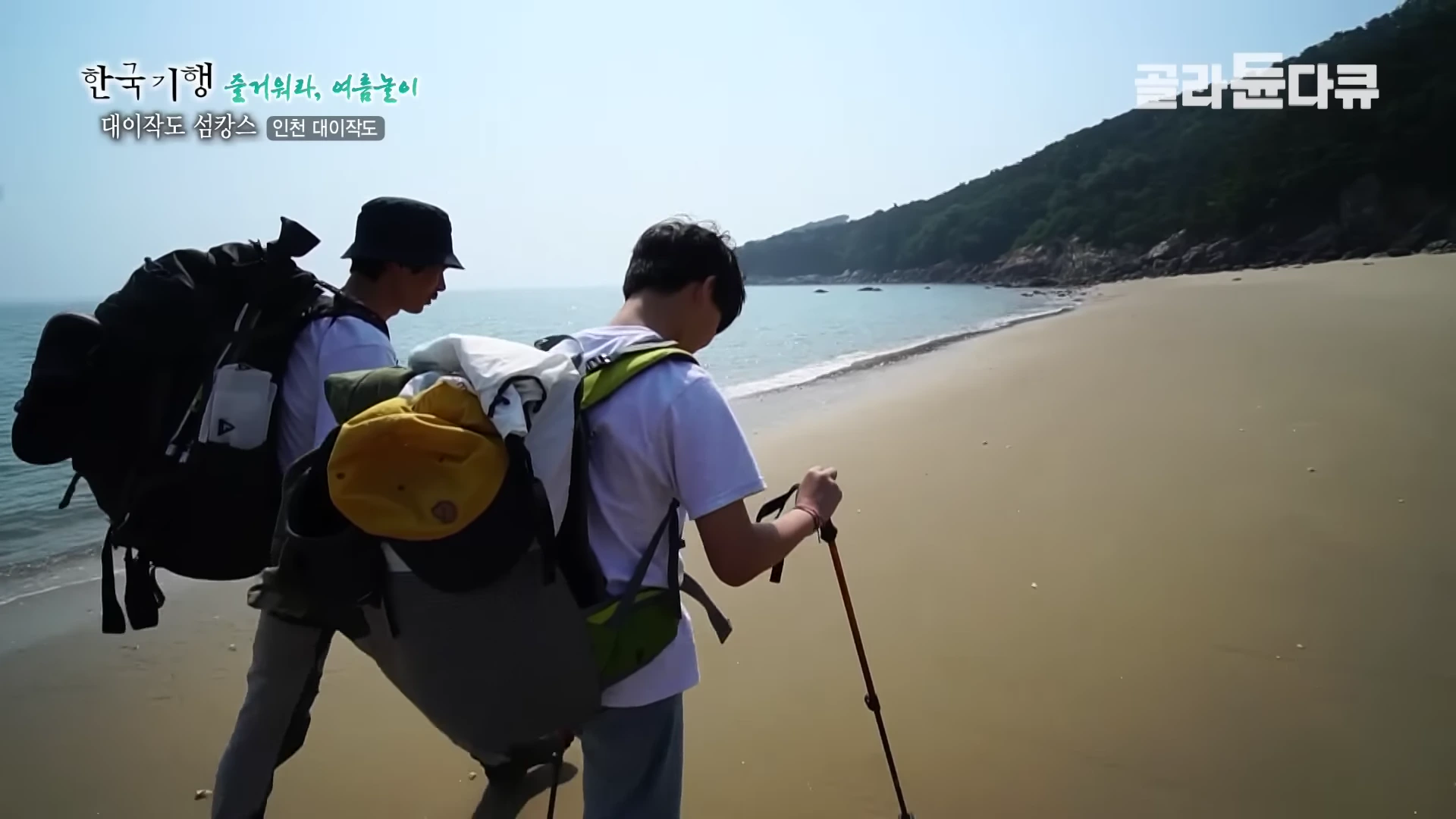 배낭을 메고 등산용 스틱을 든 두 남성이 대이작도의 모래사장 해변을 따라 걷고 있다.