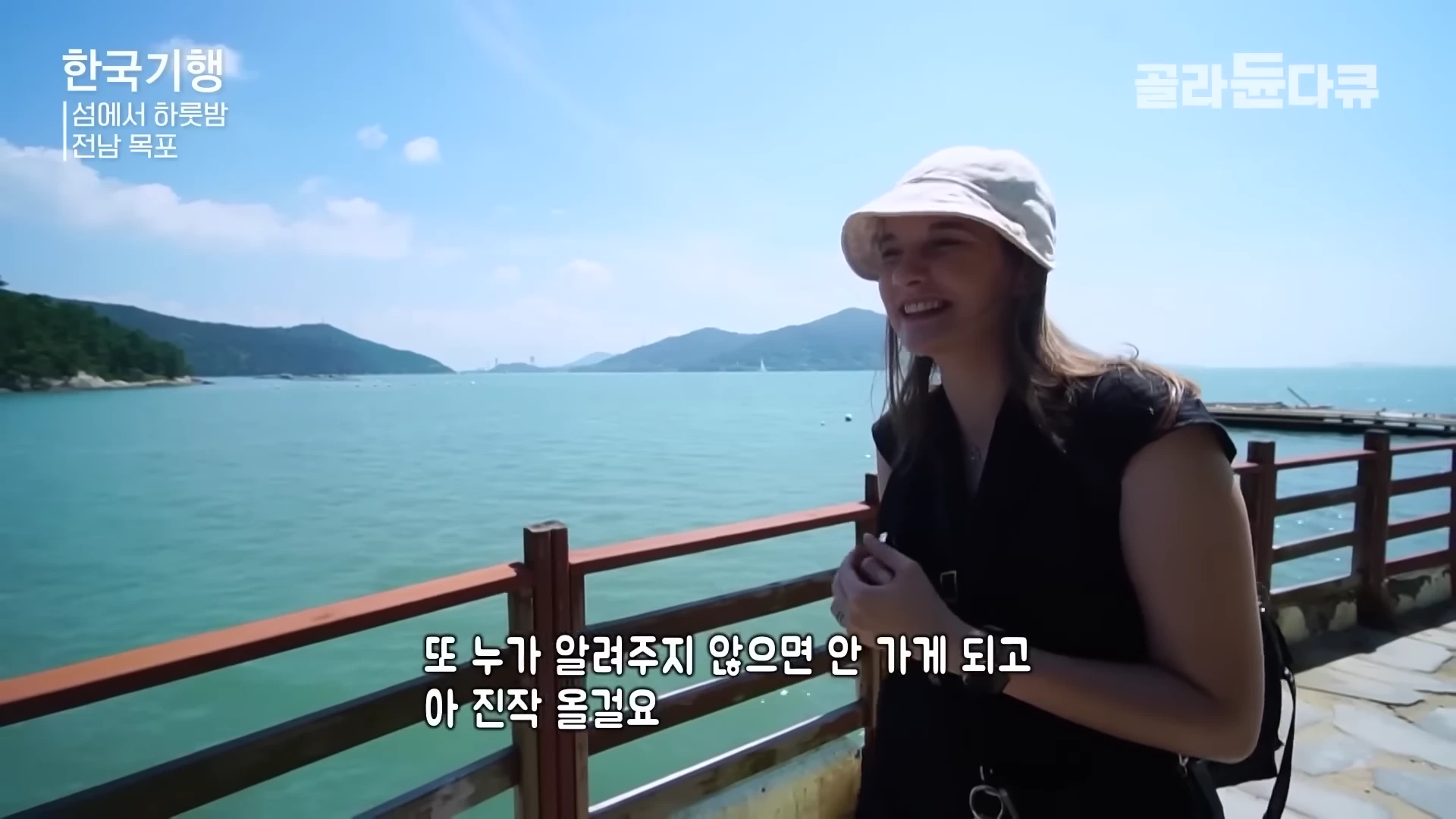 여성 여행자가 바다가 내려다보이는 난간 옆에 서서 활짝 웃고 있다.