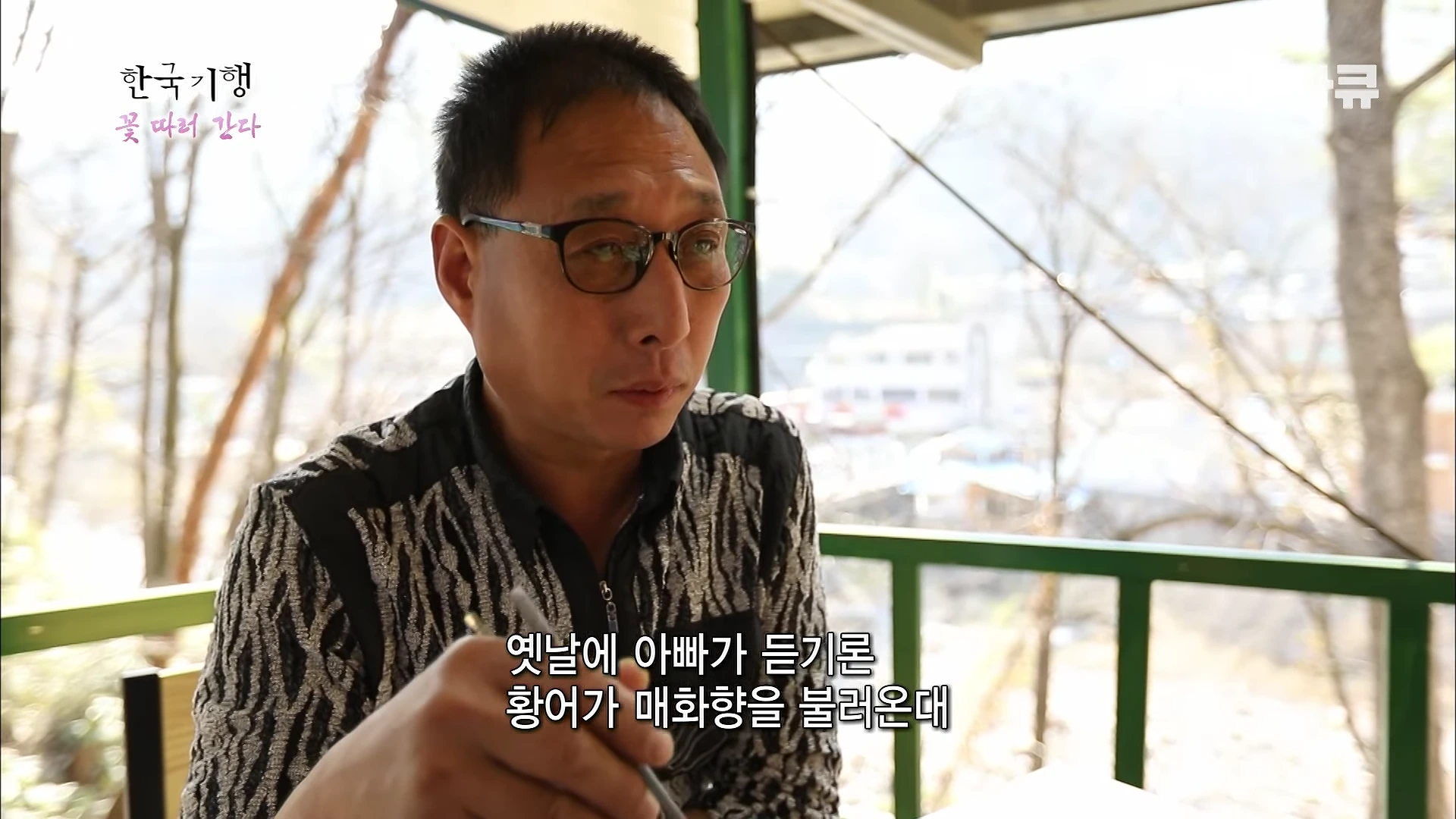 안경을 쓴 중년 남성이 야외에서 식사하며 이야기를 나누는 모습이다. 화면 하단에는 자막이 있다.
