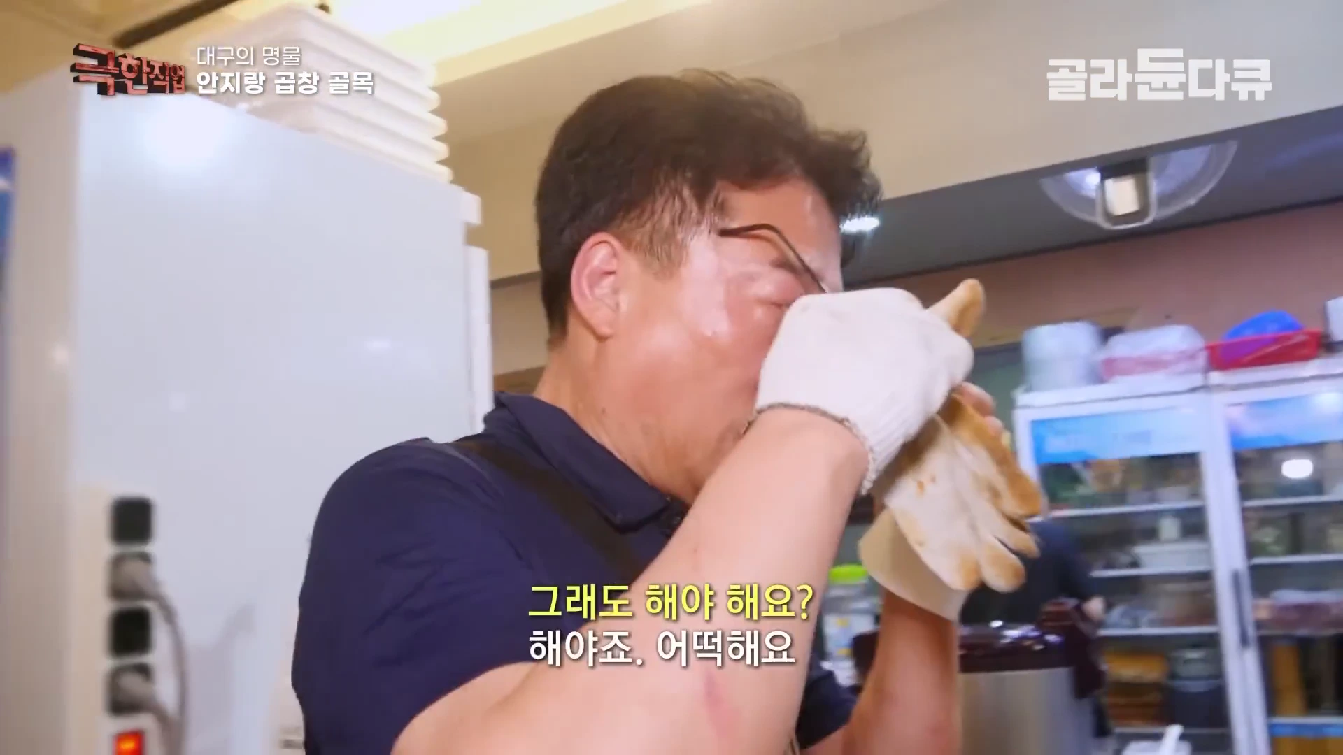 안경을 쓴 중년 남성이 화덕 열기 때문에 뜨거워진 눈을 면장갑을 낀 손으로 비비고 있는 모습