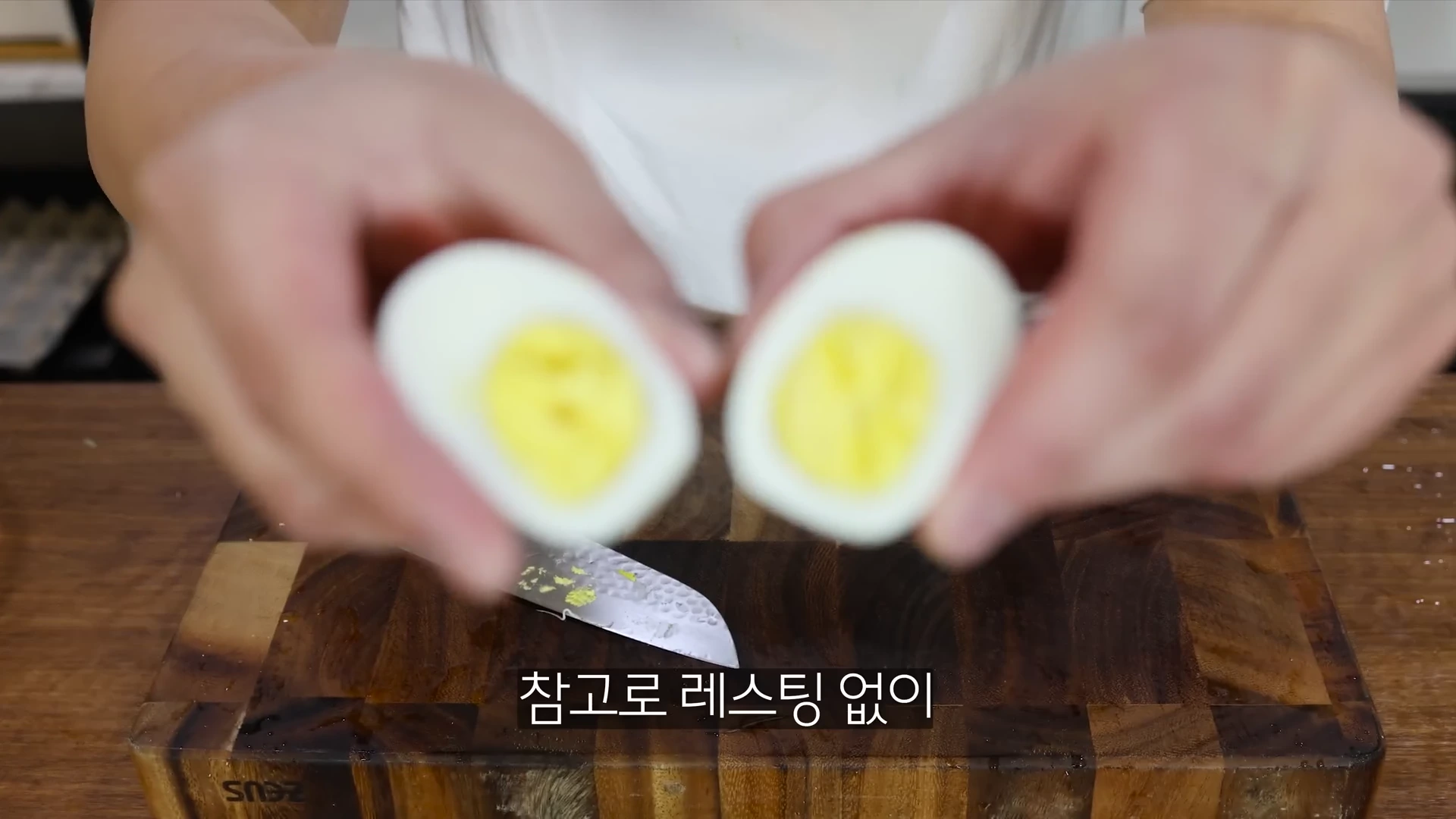 요리사가 반으로 자른 삶은 계란 두 조각을 카메라 가까이에서 보여주고 있는 모습입니다.