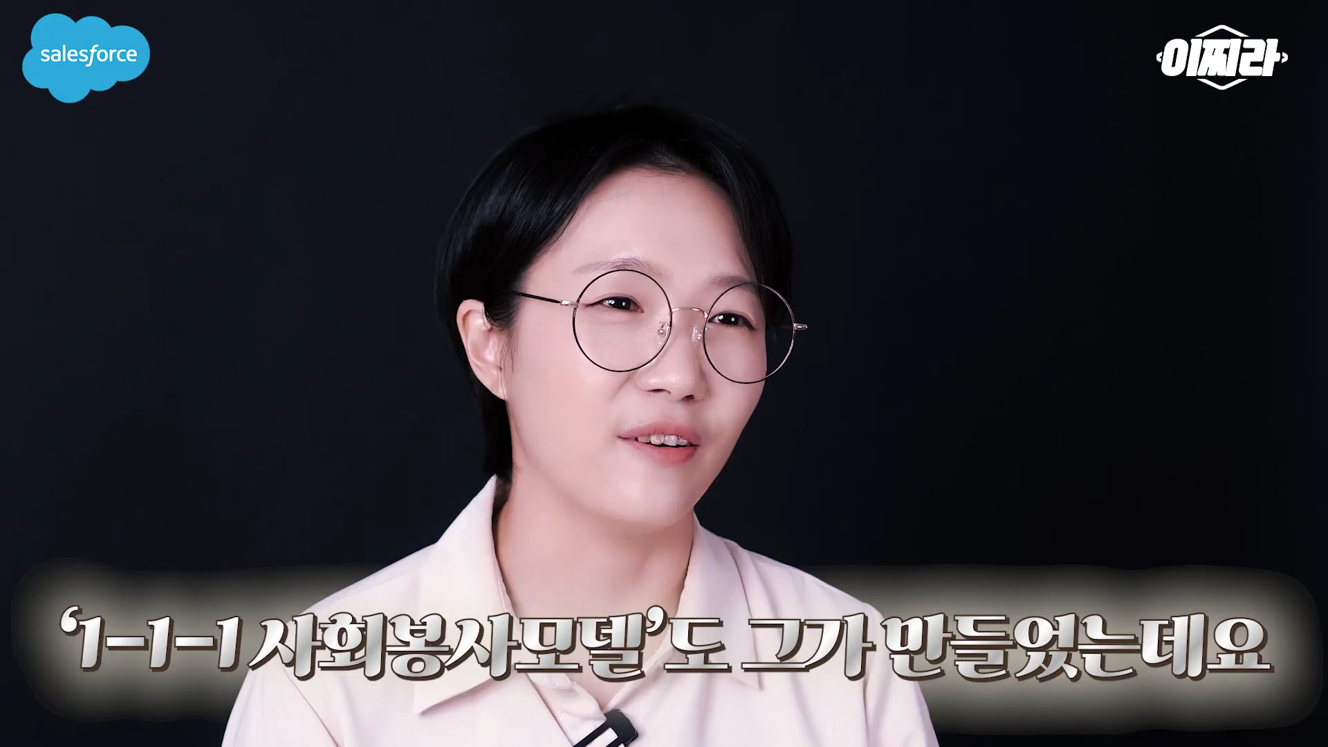짧은 머리에 안경을 쓴 여성이 검은색 배경 앞에서 화면 아래쪽에 자막이 있는 상태로 이야기를 하고 있다.