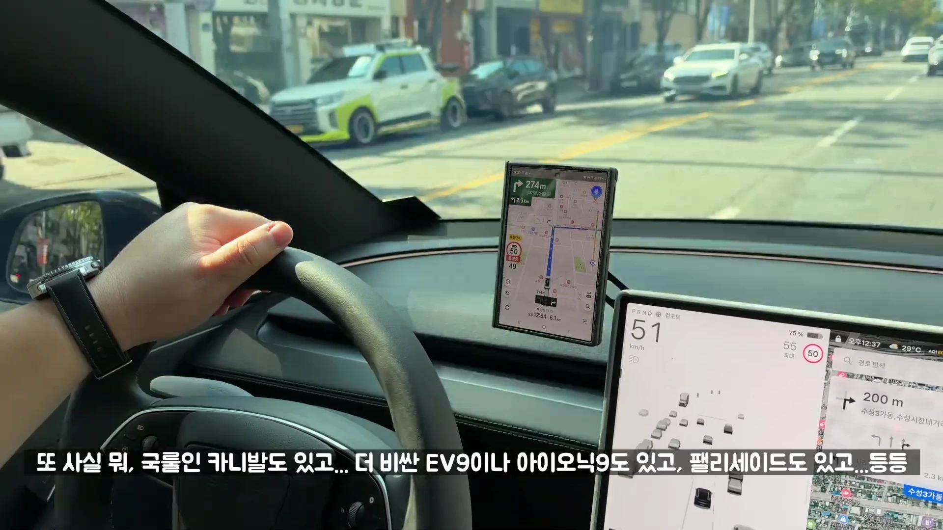 운전석에서 스티어링 휠을 잡고 도로를 주행 중인 모습으로 차량 내비게이션 화면과 스마트폰 거치대가 보입니다.
