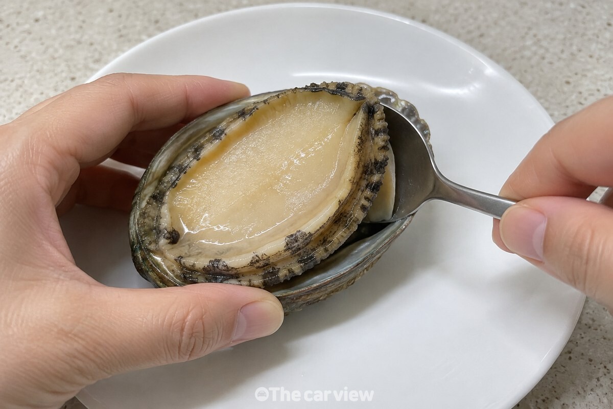 숟가락으로 껍데기 가장자리에서 전복 살을 들어 올리는 모습 / 기사 이해를 돕기 위한 생성형 이미지