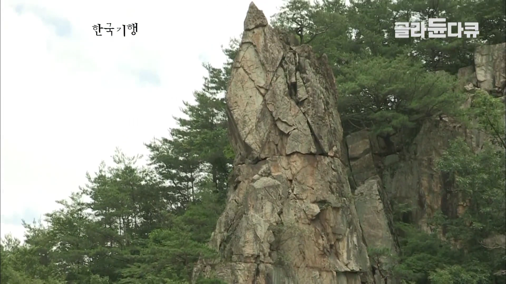 숲속에 우뚝 솟아 있는 거대한 바위인 선바위의 모습이 아래에서 위를 향해 촬영되어 있다.