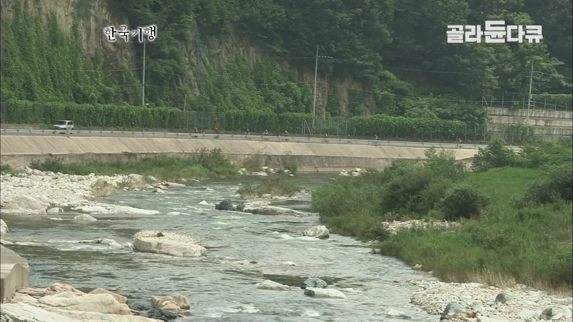 도로 옆으로 흐르는 맑은 대가천 계곡과 그 위 도로를 따라 줄지어 자전거를 타는 사람들의 모습이 담긴 풍경입니다.