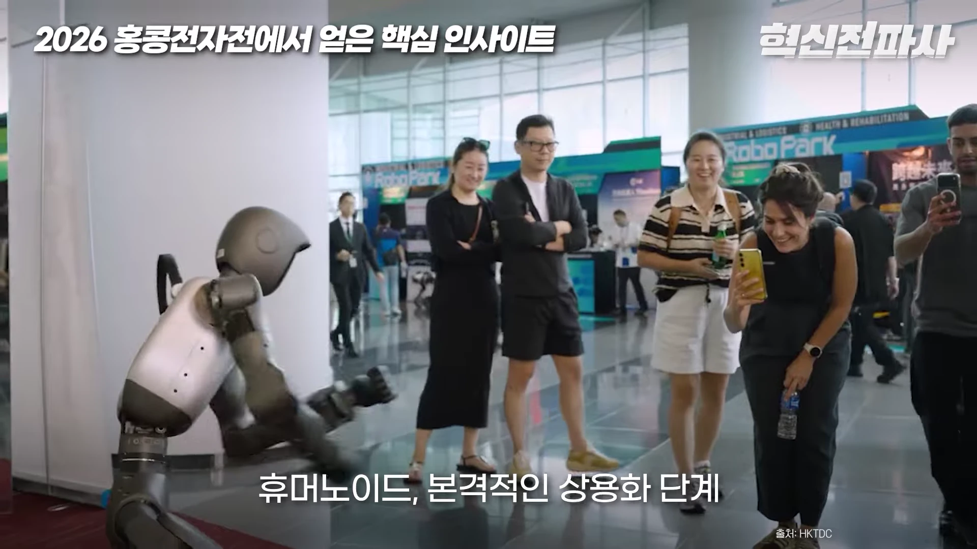 실내 전시장에서 휴머노이드 로봇이 움직이는 모습을 사람들이 스마트폰으로 촬영하며 지켜보고 있는 모습이다.