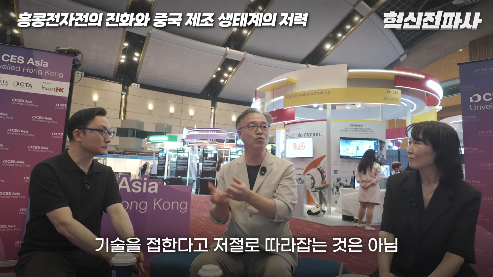 실내 전시장에서 세 사람이 의자에 앉아 대화를 나누고 있는 모습으로, 중앙에 앉은 남성이 손짓하며 말을 하고 있고 양옆에 남녀가 그 이야기를 경청하고 있습니다.