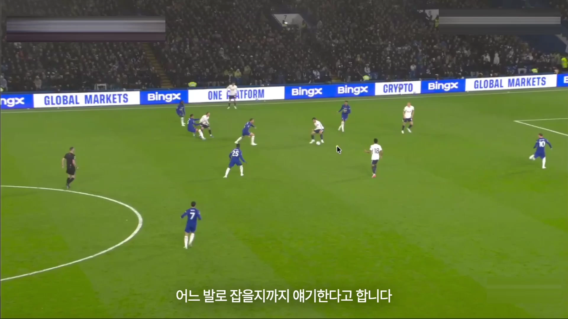 축구 경기장에서 흰색 유니폼을 입은 선수들이 공을 중심으로 모여 전술적 움직임을 보이는 모습이 담긴 화면입니다.