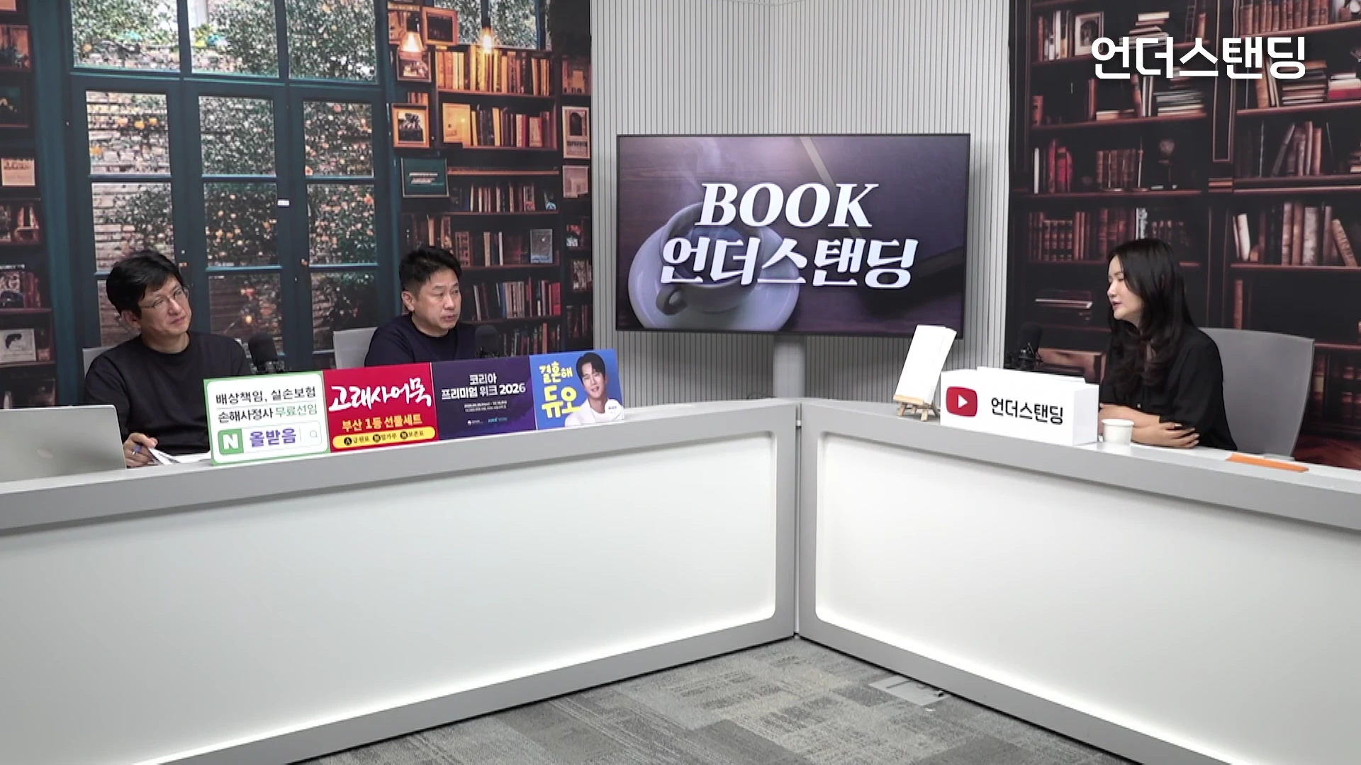 서재 배경의 스튜디오에서 진행자와 두 명의 출연자가 기역 자 형태의 책상에 앉아 대화를 나누는 모습