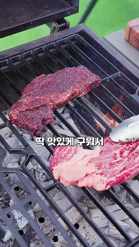 숯불 그릴 위에 커피 시즈닝이 입혀진 스테이크와 생고기 스테이크가 함께 올려져 익어가고 있는 모습이다.