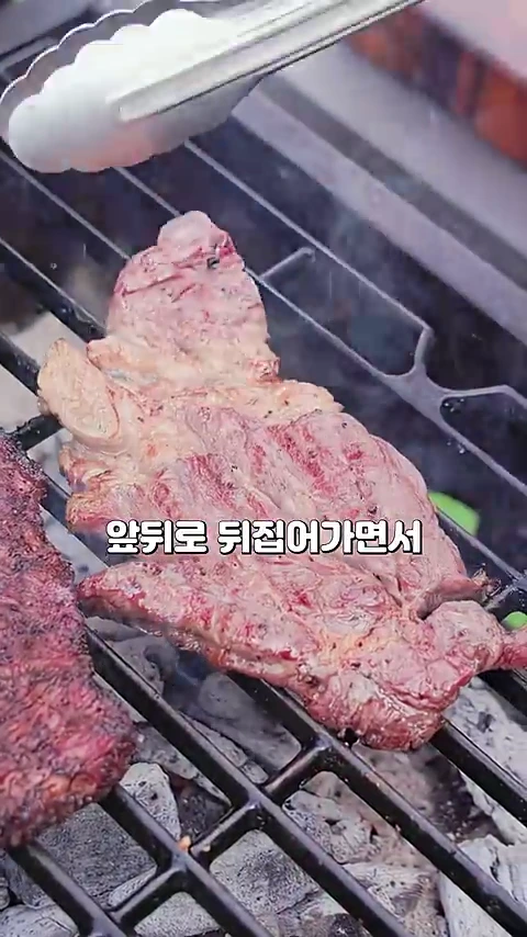 그릴 위에서 집게로 고기를 뒤집고 있는 모습