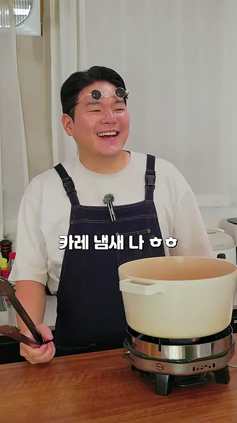 앞치마를 두르고 선글라스를 머리에 얹은 남성이 환하게 웃으며 요리하고 있는 모습