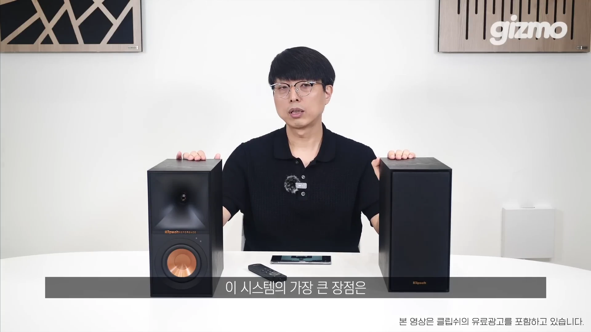 흰색 배경의 스튜디오에서 안경을 쓴 남성이 양옆에 검은색 스피커 한 쌍을 놓고 설명하고 있다.