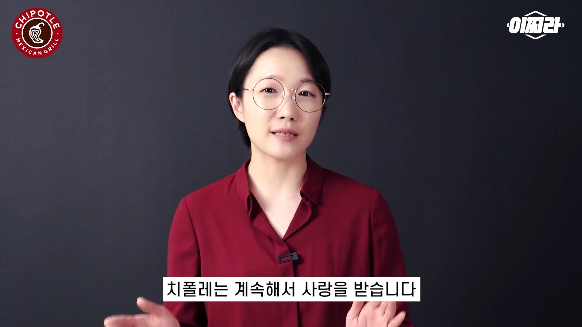 단발머리에 안경을 쓴 여성이 검은 배경 앞에서 이야기를 하고 있는 모습