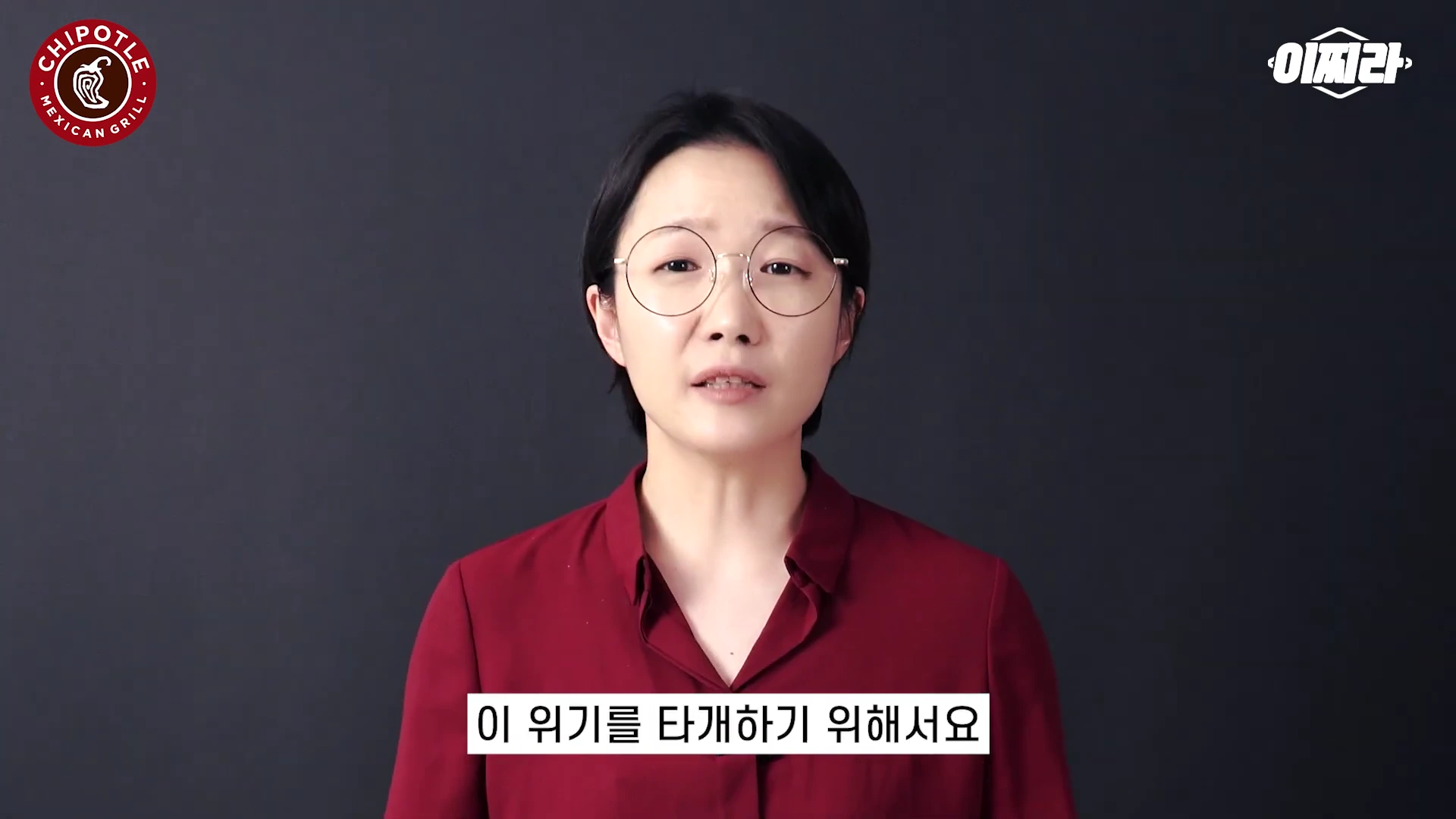 안경을 쓴 단발머리의 여성 진행자가 붉은색 셔츠를 입고 검은색 배경 앞에서 무언가를 설명하고 있는 영상의 한 장면입니다.
