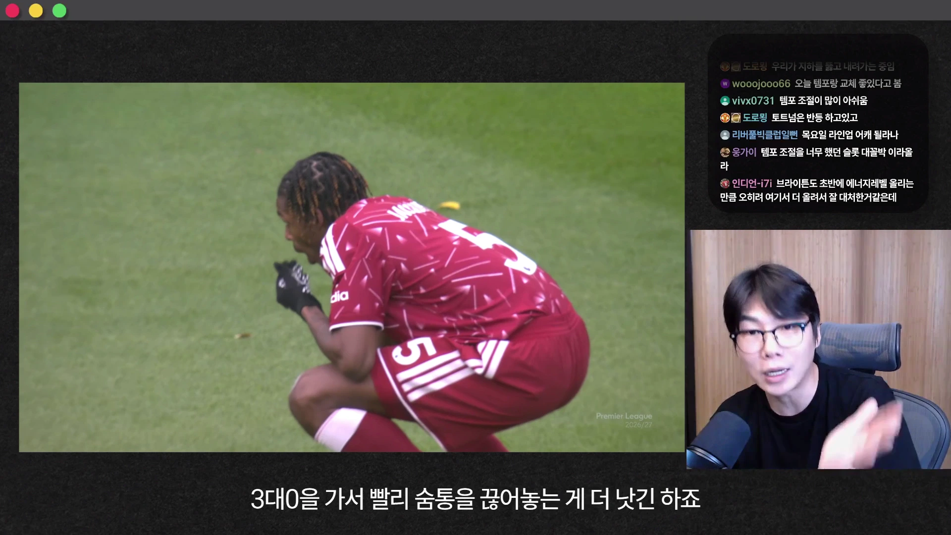 축구 경기 중 한 선수가 그라운드 위에 웅크리고 앉아 있는 모습과 화면 우측에서 안경을 쓴 남성이 마이크를 향해 말하는 모습이 담긴 영상 캡처 화면입니다.
