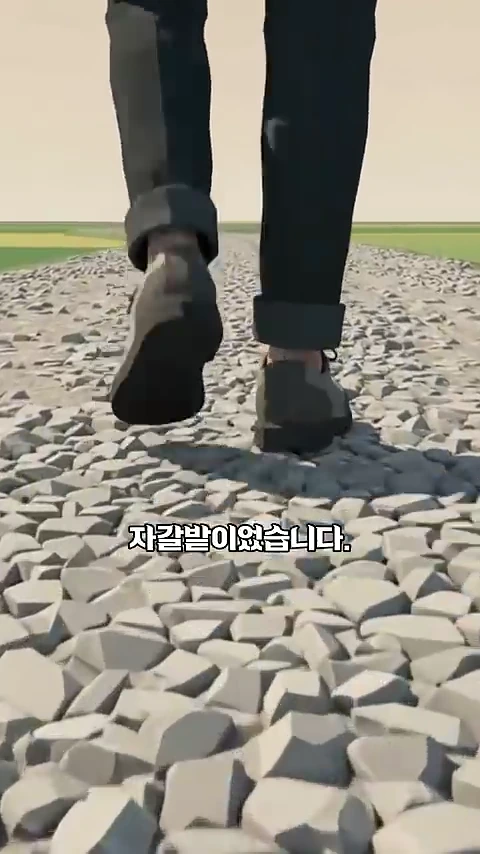 바지 끝단을 접어 올린 사람이 울퉁불퉁한 자갈밭 위를 걷는 모습을 아래에서 위로 비춘 장면.