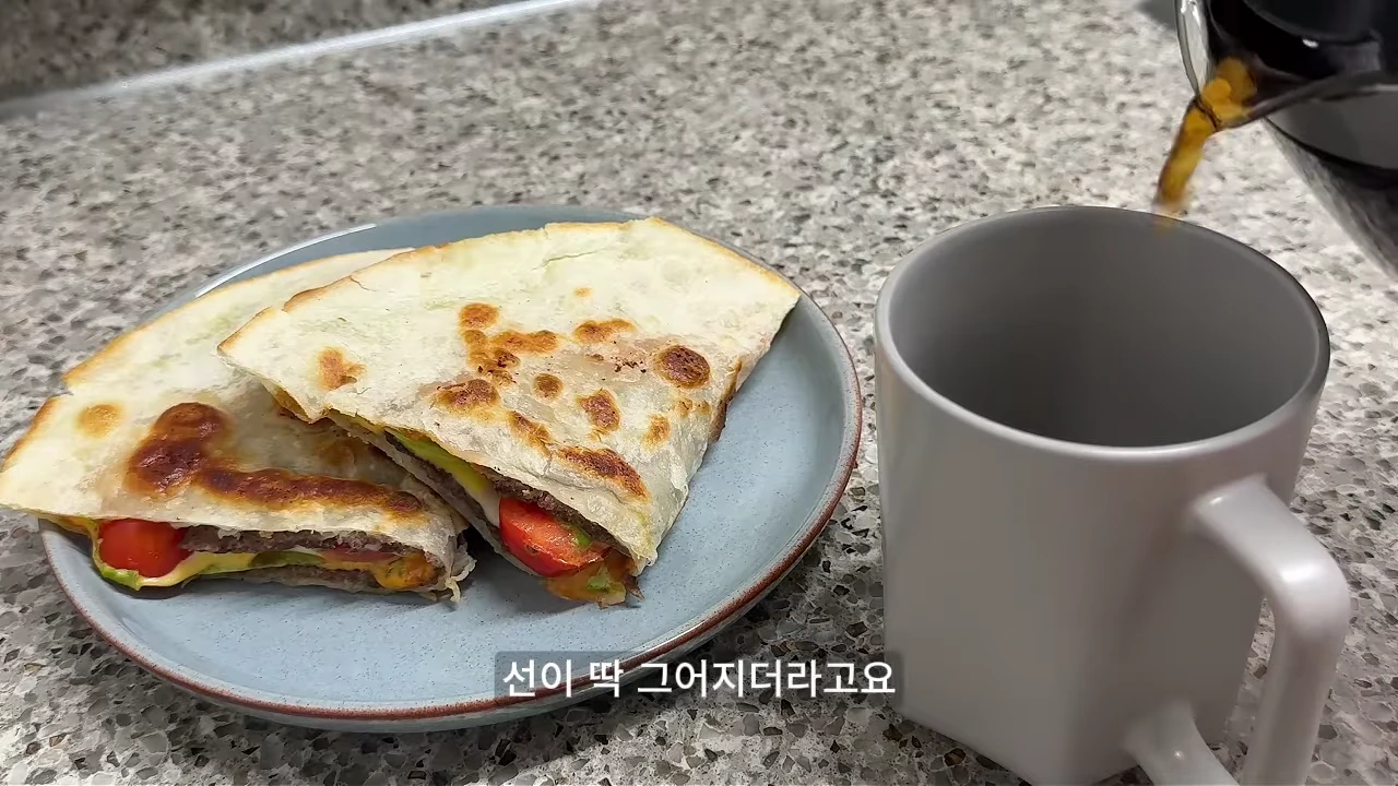 그레이 톤의 접시에 담긴 퀘사디아와 옆의 머그잔에 음료가 따라지고 있는 모습