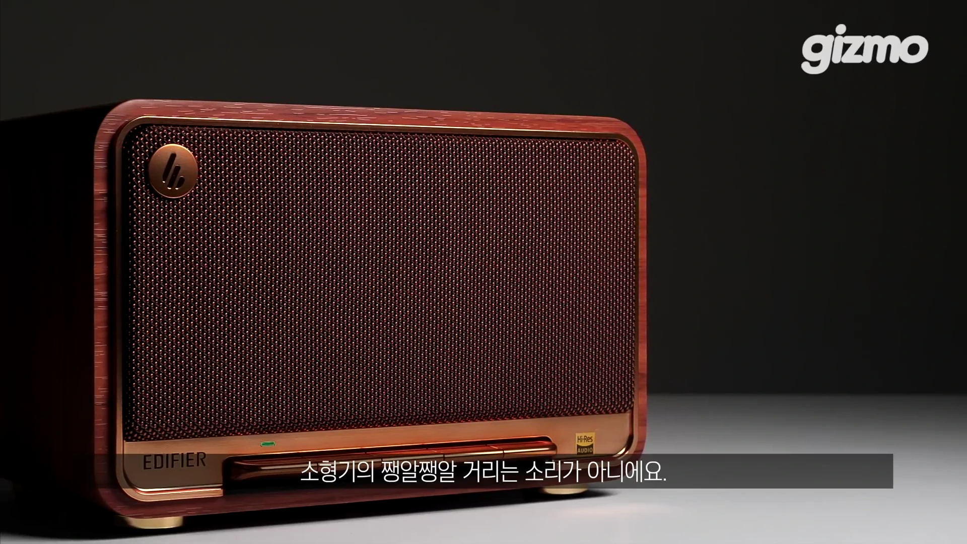 나무 무늬 질감의 본체와 금색 테두리가 돋보이는 레트로 디자인의 직사각형 스피커가 어두운 배경에 놓여 있다.