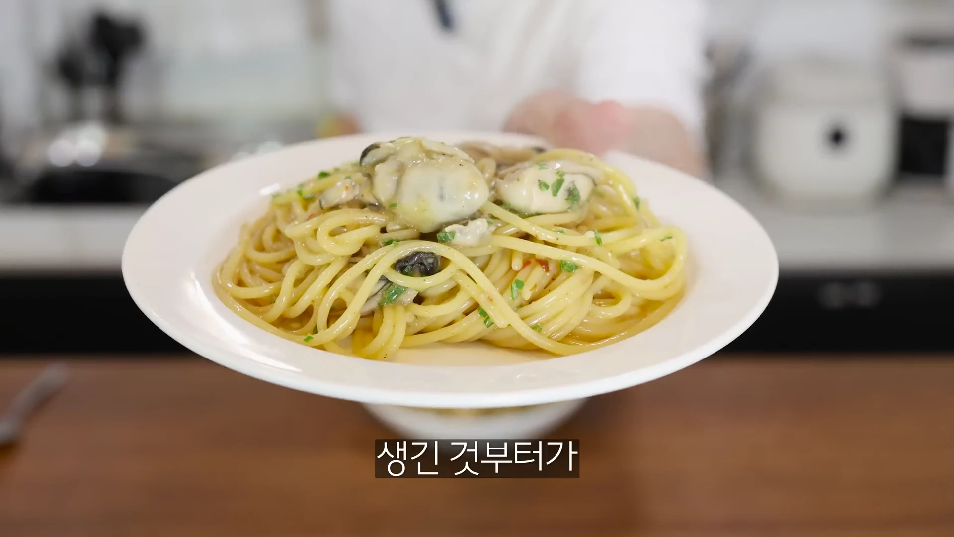 흰 접시에 담긴 굴 파스타를 손으로 들어 보여주는 모습