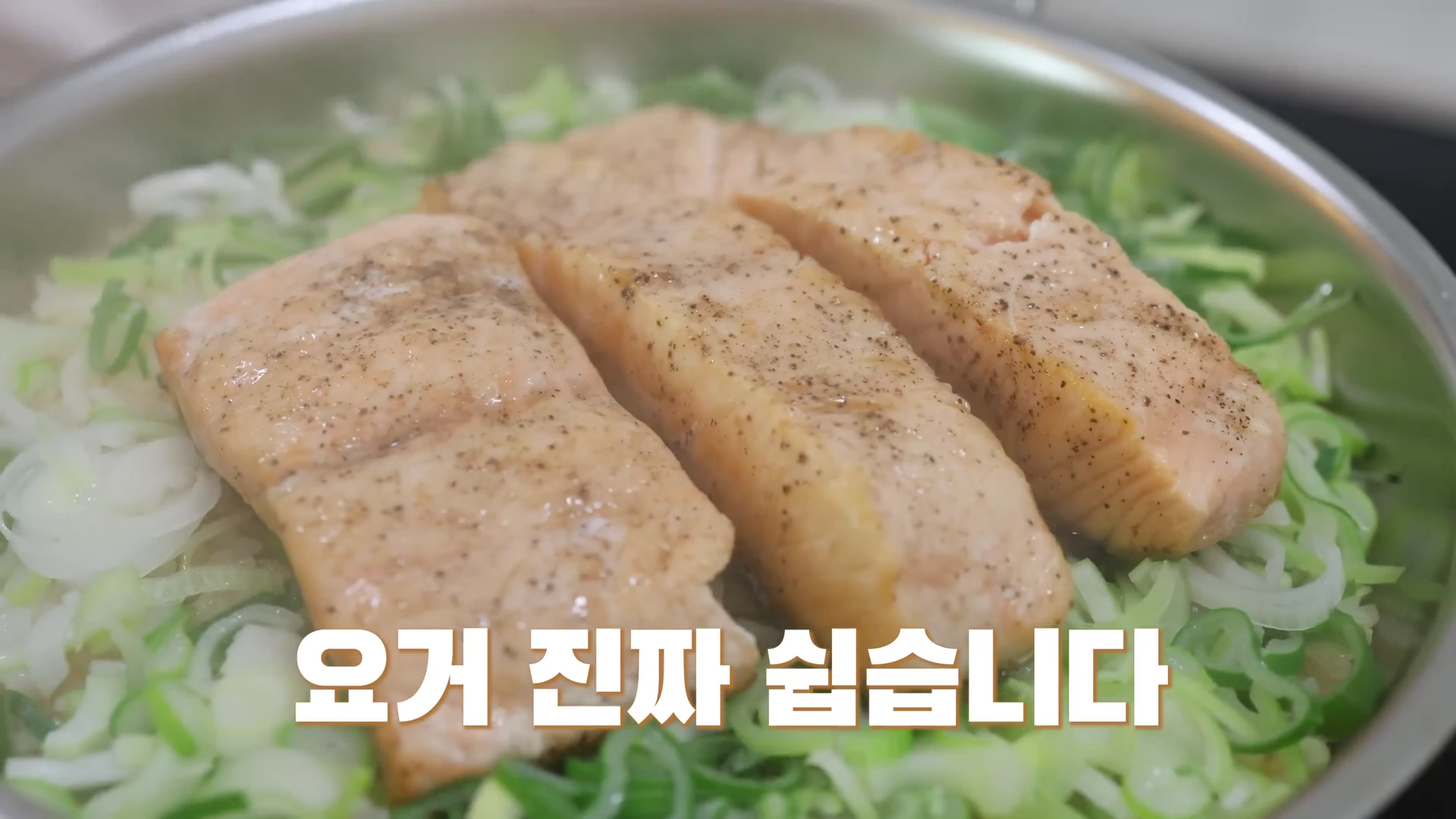 프라이팬 위에서 잘게 썬 대파와 함께 구워지고 있는 세 덩이의 연어 스테이크와 '요거 진짜 쉽습니다'라는 흰색 자막.