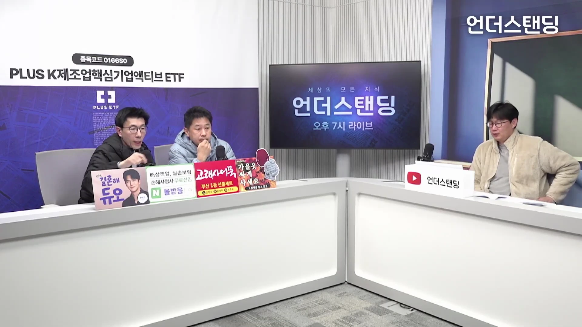 스튜디오에 세 명의 남성이 책상을 사이에 두고 앉아 대화를 나누고 있는 모습.