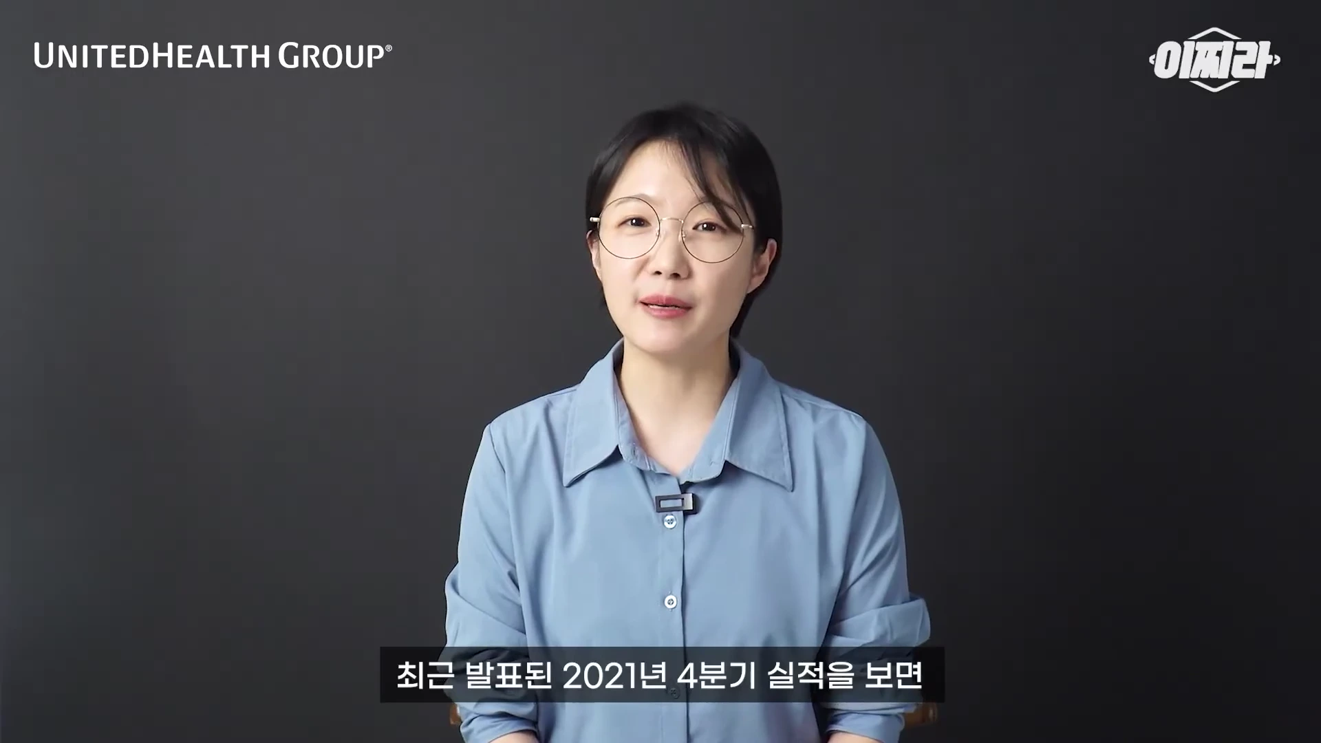 안경을 쓴 여성이 검은색 배경 앞에서 정면을 응시하며 이야기하고 있는 모습의 영상 화면이다. 화면 상단에는 기업 로고와 채널명이 표기되어 있고, 하단에는 한국어 자막이 노출되어 있다.