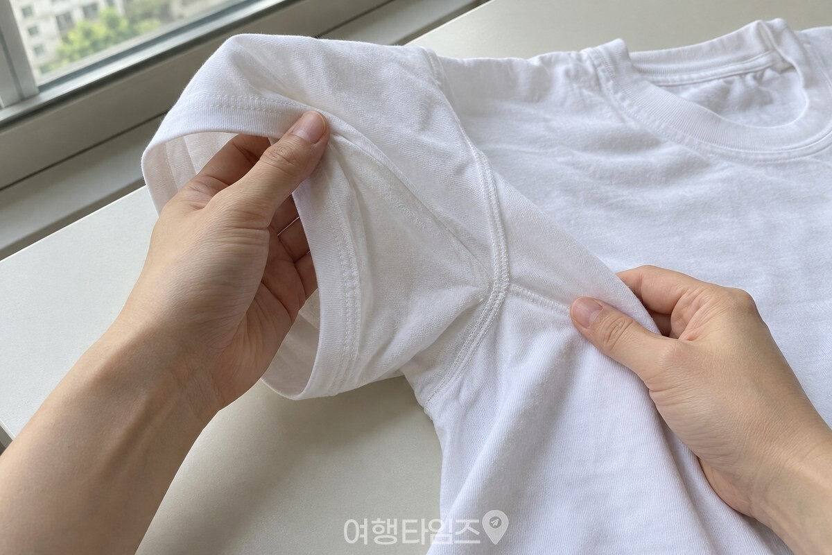 밝은 창가에서 겨드랑이 부분을 펼쳐 확인하는 흰 면 티셔츠 / 기사 이해를 돕기 위한 생성형 이미지
