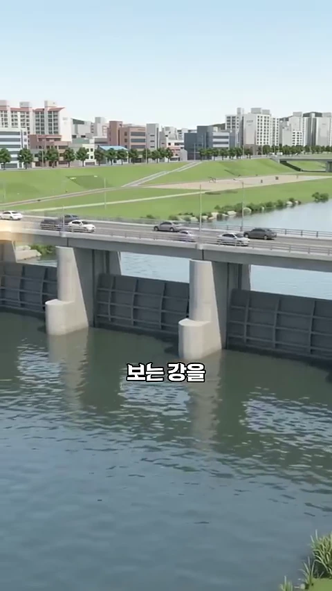 강물을 가로질러 설치된 회색 콘크리트 보와 그 위로 자동차들이 지나가는 다리가 보이며, 화면 중앙에는 '보는 강을'이라는 한글 자막이 적혀 있습니다.