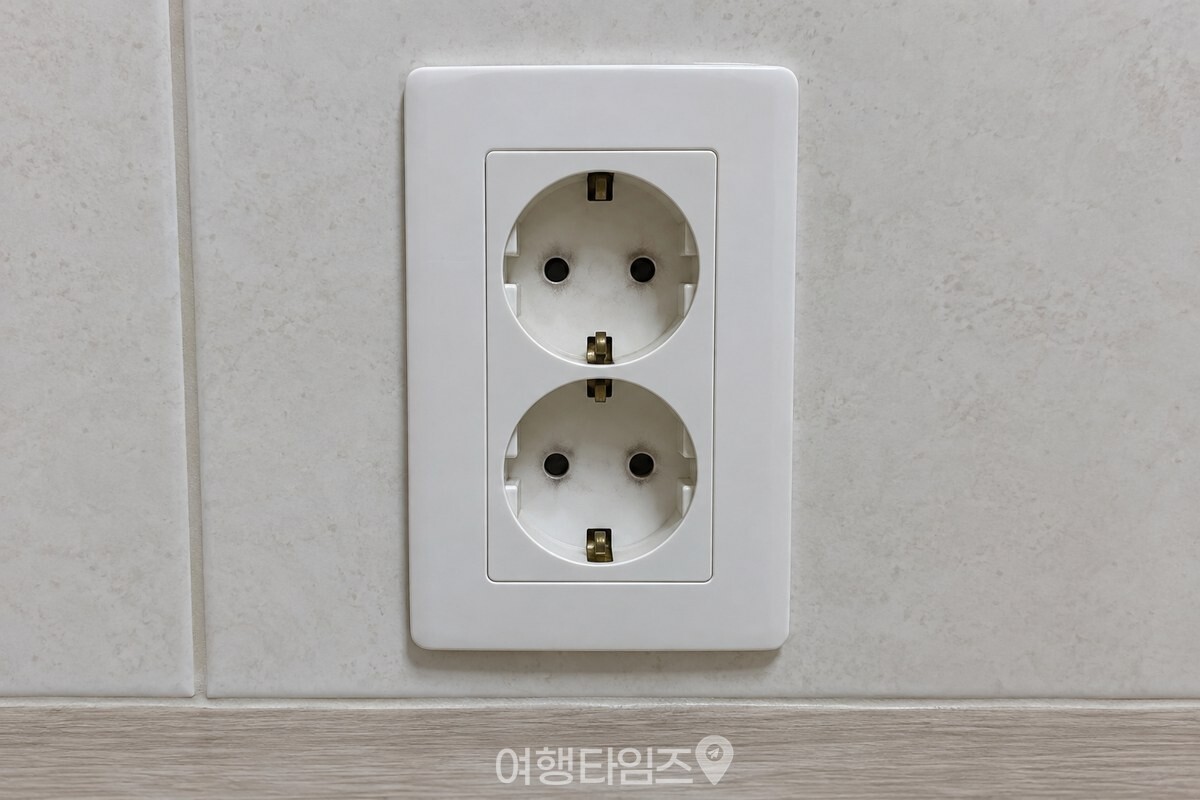 플러그를 뽑은 벽 콘센트 구멍 둘레의 옅은 먼지 / 기사 이해를 돕기 위한 생성형 이미지