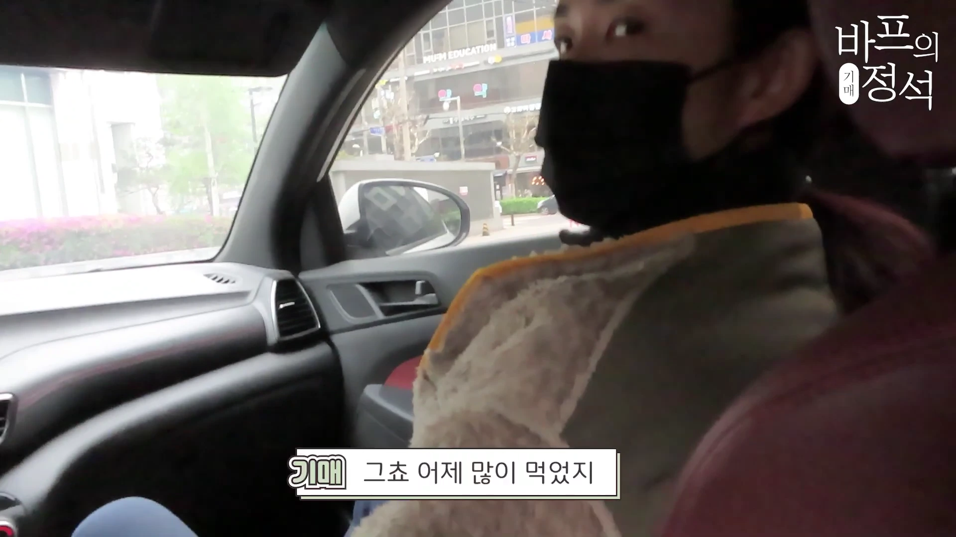 차량 조수석에 앉아 카메라를 바라보는 검은색 마스크를 착용한 인물의 측면 모습.