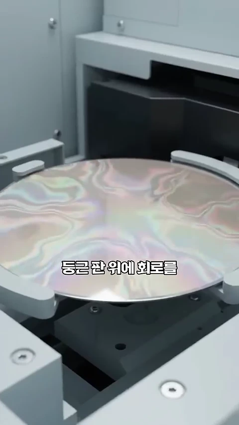 금속 장비에 고정되어 있는 반짝이는 원형의 웨이퍼가 클로즈업된 화면
