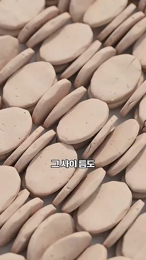 균일하게 납작하게 눌린 찰흙 조각들이 겹겹이 쌓여 있는 모습이 담긴 클로즈업 영상 캡처 화면이며, 중앙에 '그사이틈도'라는 자막이 적혀 있습니다.