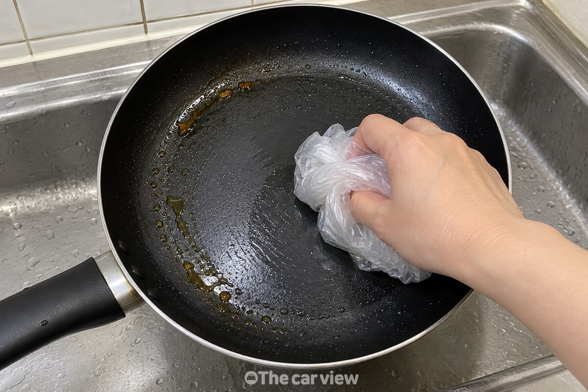 물기가 남은 프라이팬 바닥을 뭉친 비닐봉지로 닦는 손 / 기사 이해를 돕기 위한 생성형 이미지