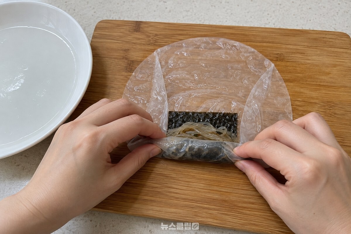 김과 당면을 올린 라이스페이퍼를 말아 끝을 누르는 손 / 기사 이해를 돕기 위한 생성형 이미지