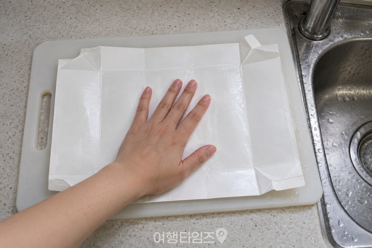 도마 위에 펼친 우유팩을 손바닥으로 누르는 모습 / 기사 이해를 돕기 위한 생성형 이미지
