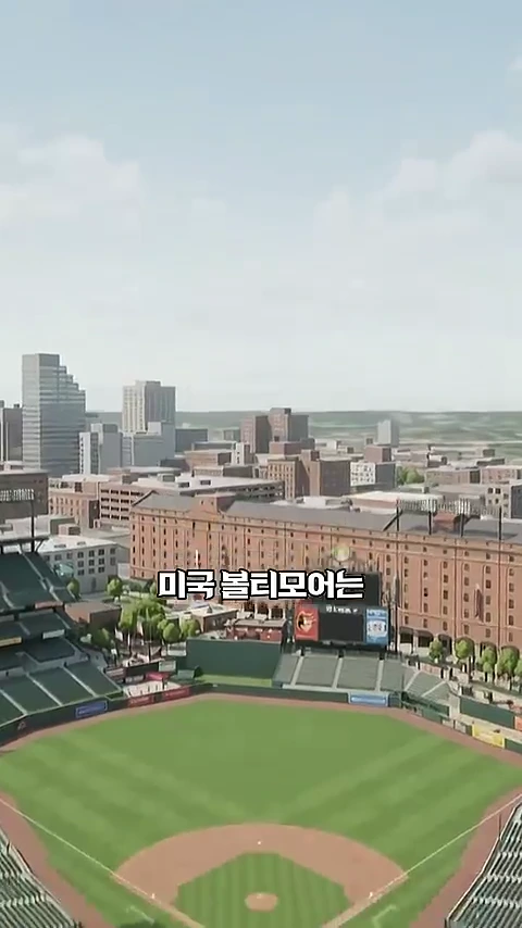 하늘에서 내려다본 야구장 전경으로 초록색 잔디 구장 뒤편에 낮은 벽과 벽돌 건물들이 자리 잡고 있으며 한국어 자막이 화면 중앙에 배치되어 있다.